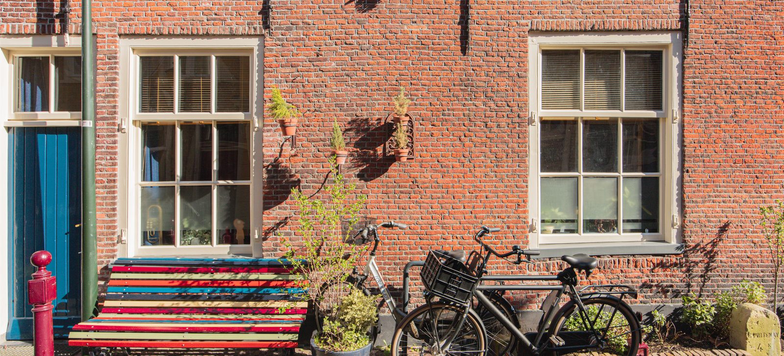 Bakstenen gevel van een woonhuis met een bankje en fietsen ervoor