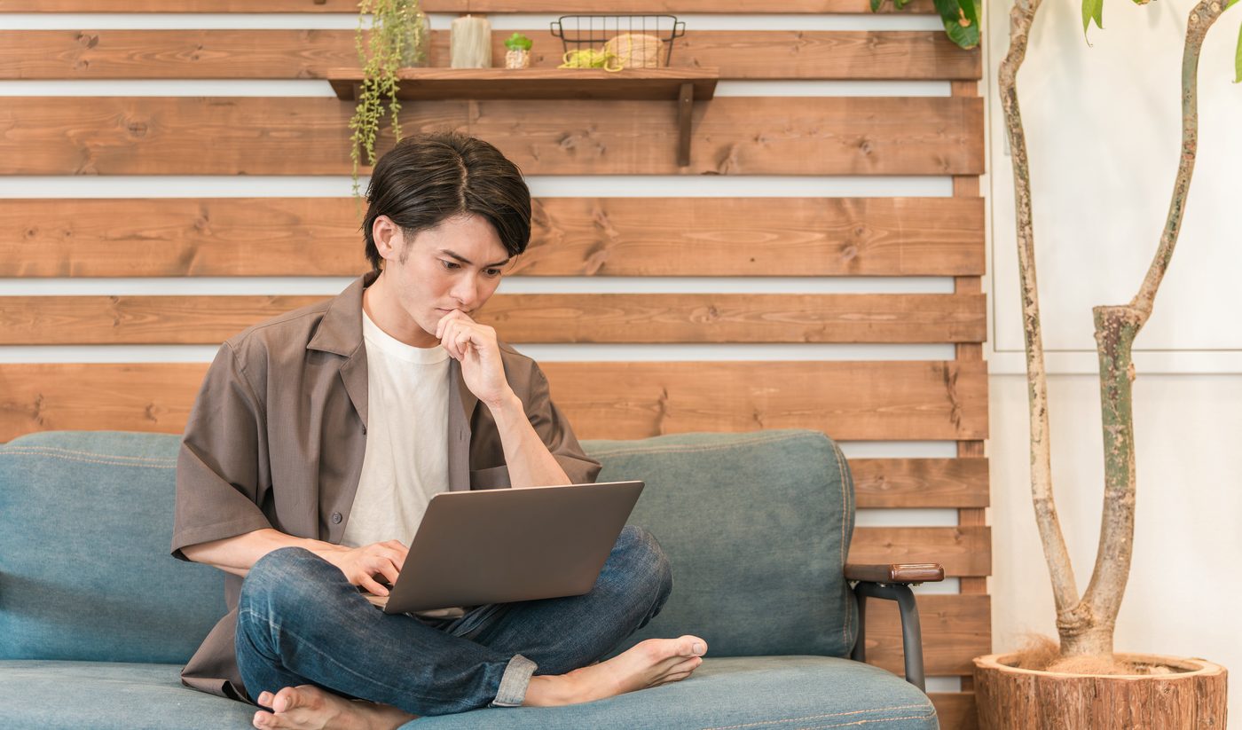 Jongere zit ontspannen op de bank met een laptop in de gemeenschappelijke woonkamer