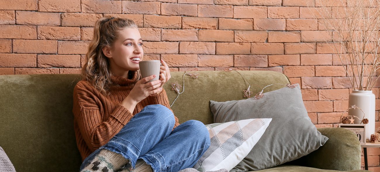 Jonge vrouw met een mok thee op de bank tegen een bakstenen muur